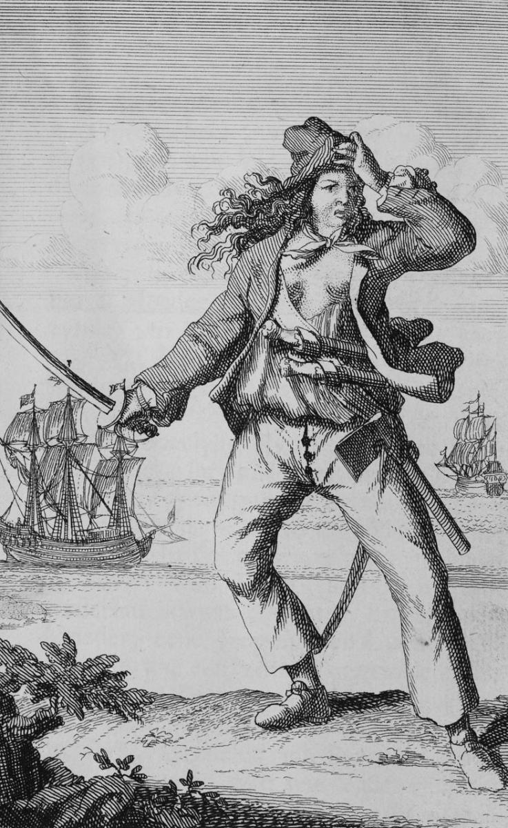 Pirate Mary Read stands on the shore brandishing a sword. A pirate ship is at sea behind her.