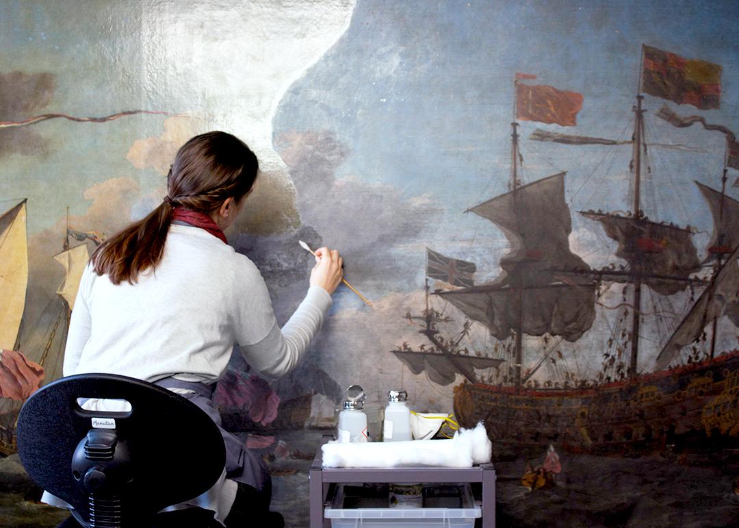 A conservator works on a small portion of a large maritime oil painting