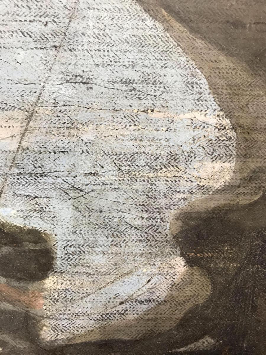 Close-up photo of the surface of a painting before conservation work. Black marks and scratches are visible in the light paint