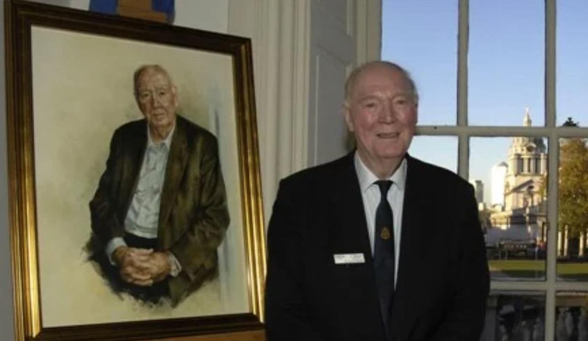 Sir David Hardy posing next to his painted portrait