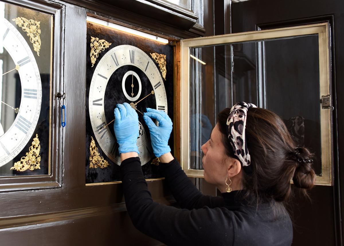 A women wearing blue surgical gloves makes adjustments to a historic clock face as part of conservation work at the Royal Observatory