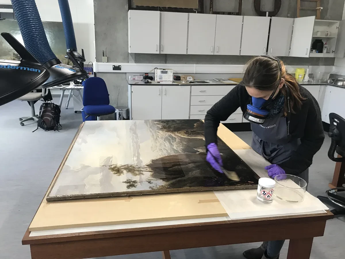 A painting conservator applies a varnish to a painting