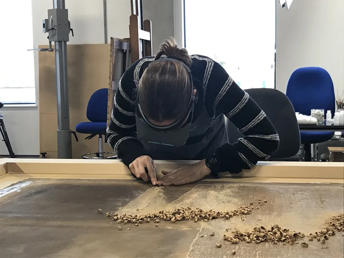 A painting conservator carefully scrapes away the old lining canvas of a painting