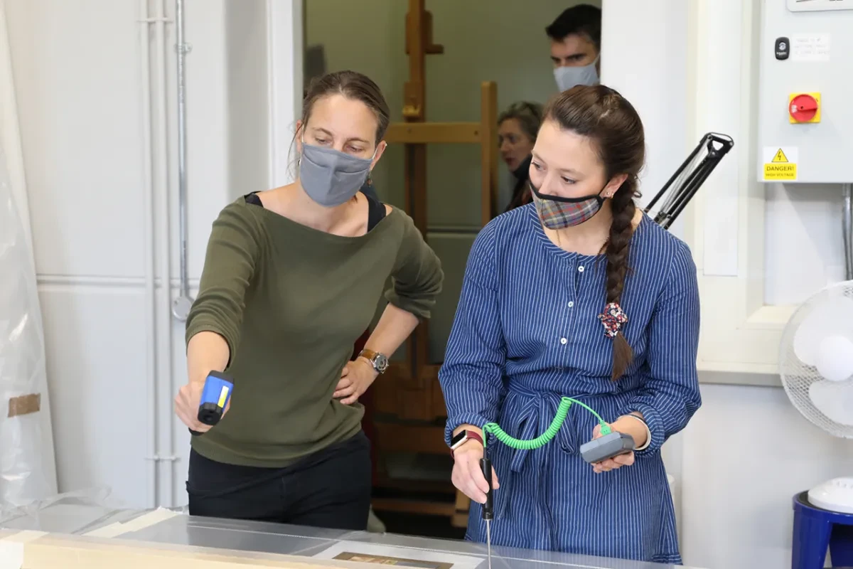 A painting conservator takes a temperature reading of the surface of a painting during conservation treatment