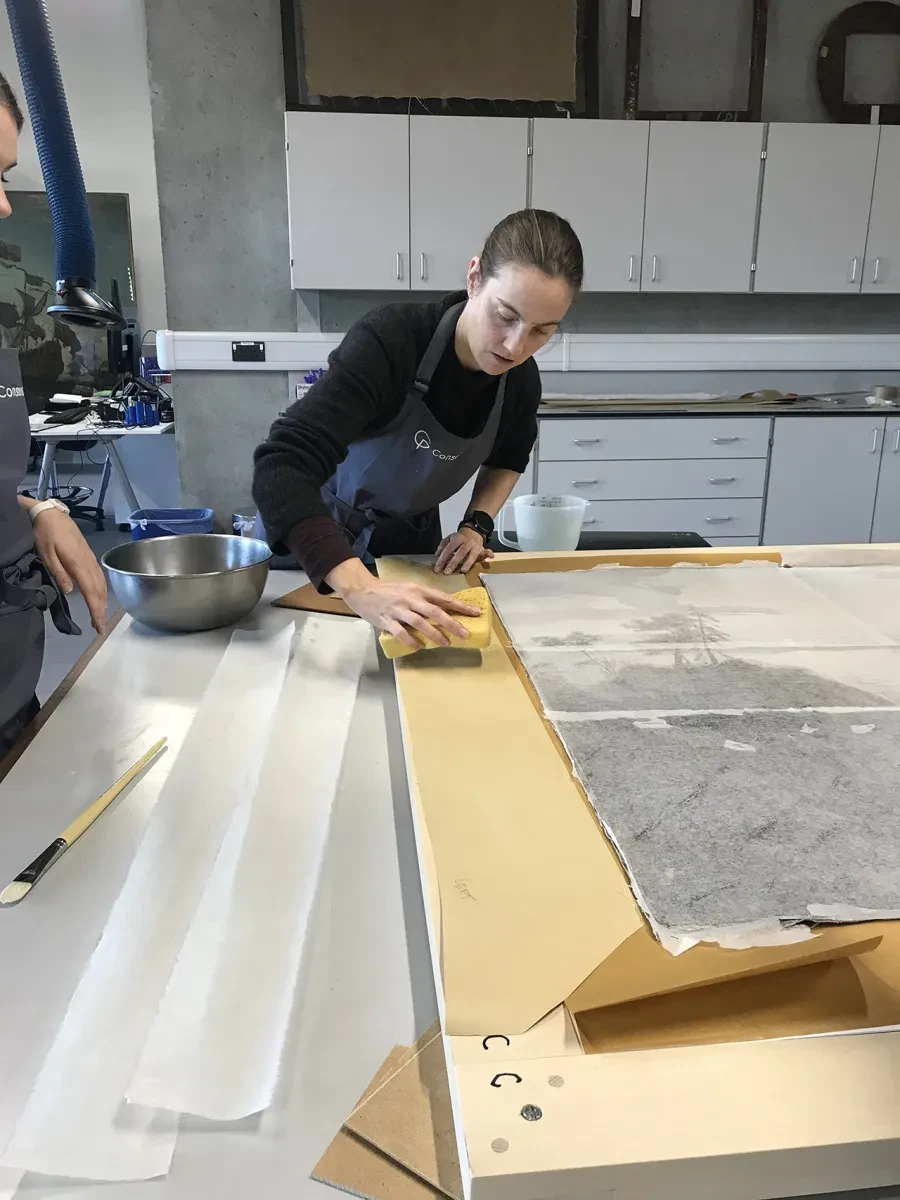 A painting conservator wipes down Kraft paper to keep it damp during a conservation project
