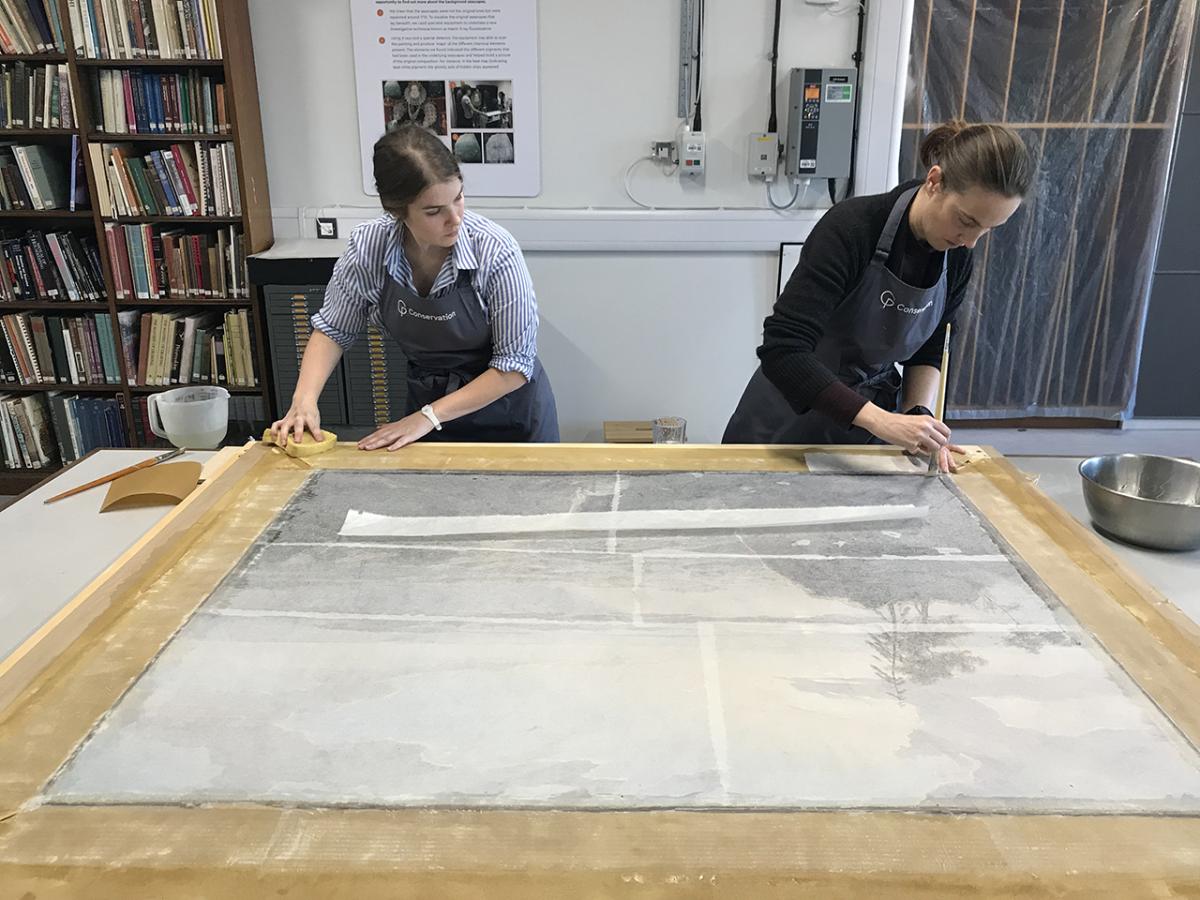 Two conservators examine the reverse of a painting during a conservation project