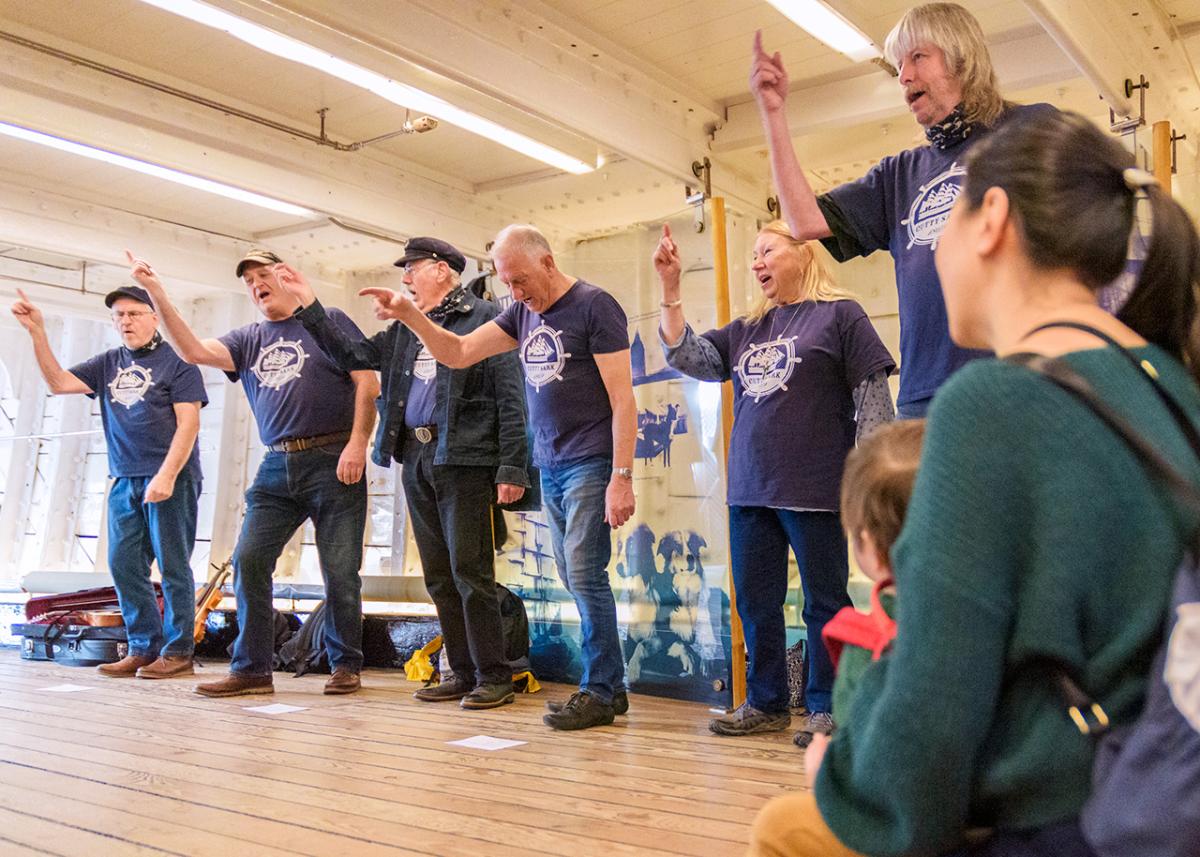 A mum and her child watch on as a group of sea shanty singers perform at historic ship Cutty Sark