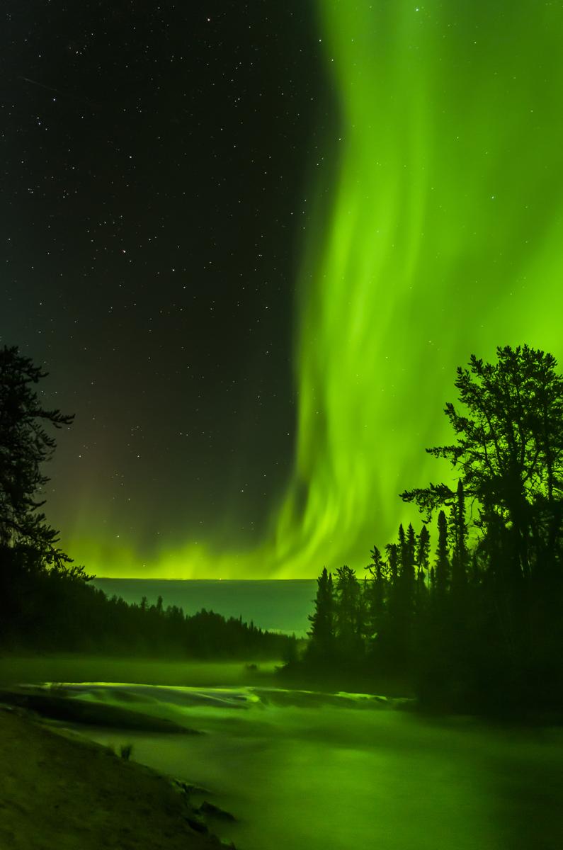 Green aurorae over the misty Cameron River in Canada
