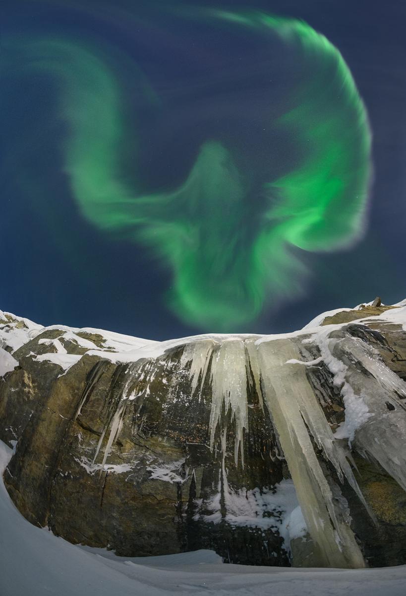Green eagle shaped aurora over snow capped mountain