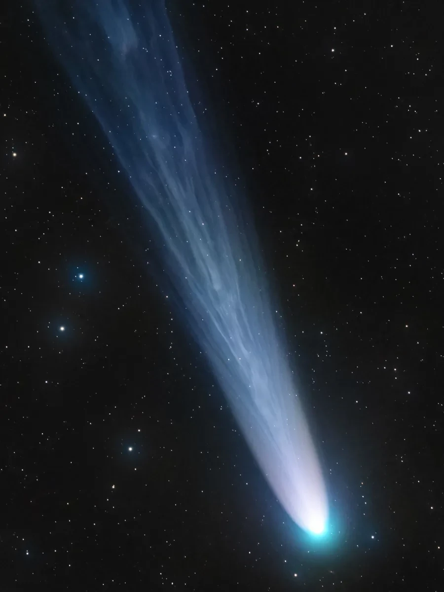 Portrait image of long, light blue and white comet against a black starry background