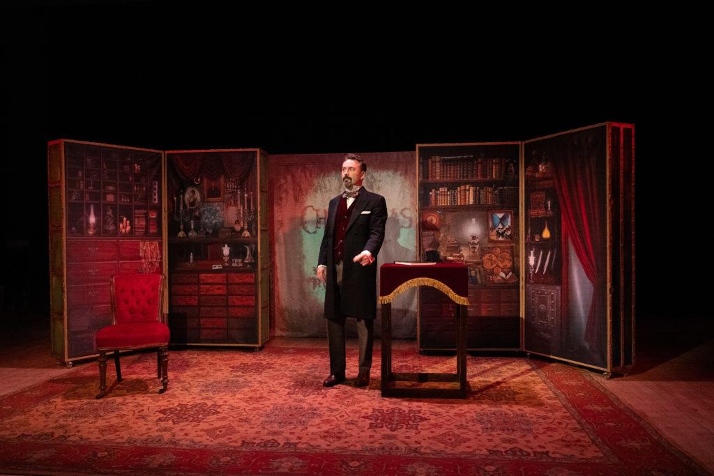 Image of theatre set with man dressed in 1800s clothing in a library