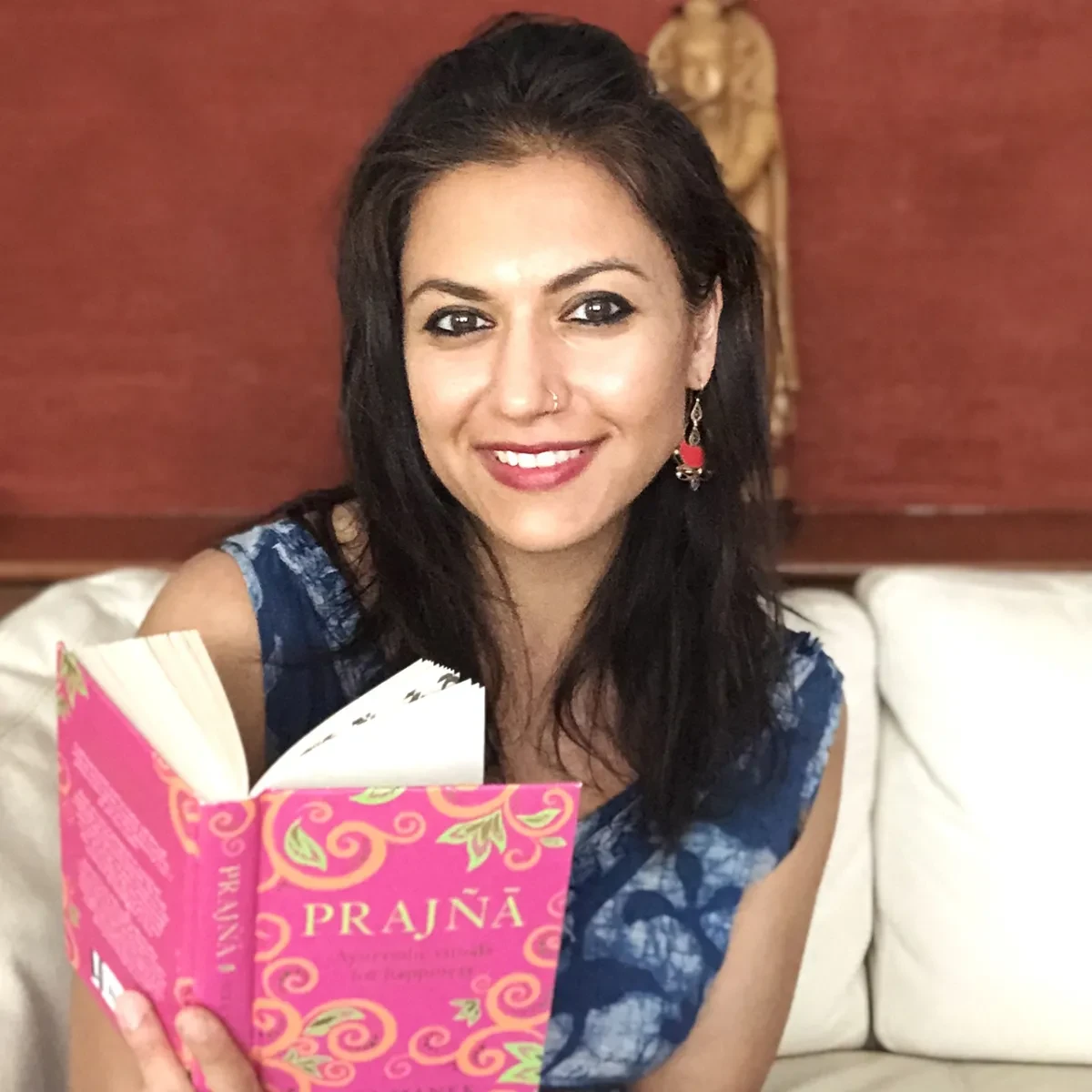A profile photo of author and chef Mira Manek. She is holding her book with the title Prajna visible on the front cover