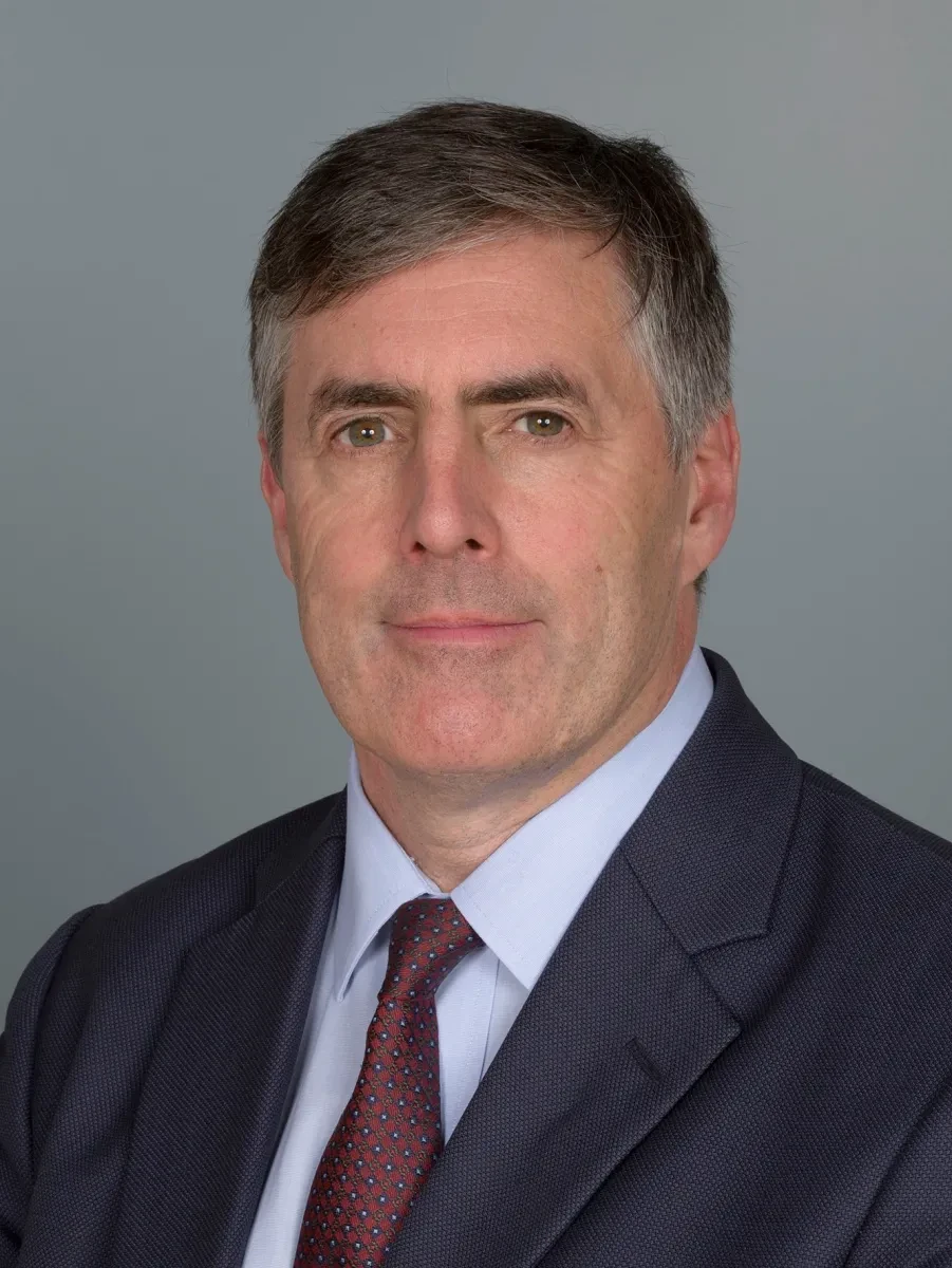 A portrait photograph of Royal Museums Greenwich Chairman Lance Batchelor. He is wearing a dark navy suit and a tie with a red and blue geometric pattern