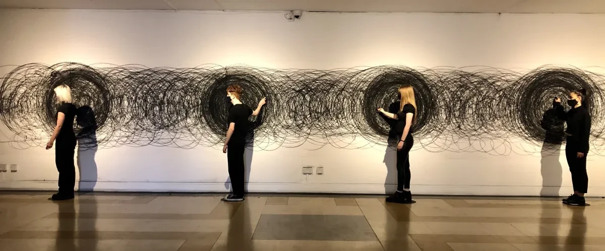Four people wearing black draw black circles on a wall.