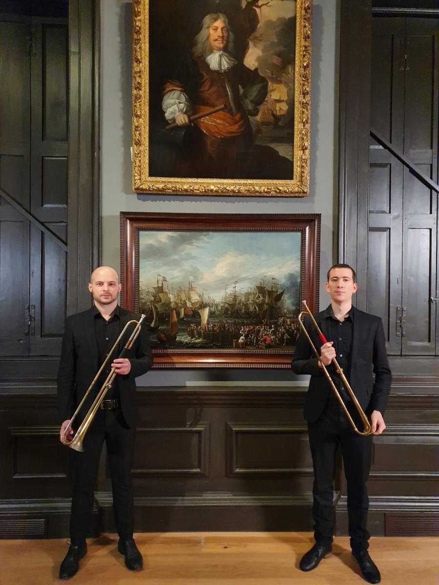Two trumpeters standing next to a painting showing a fanfare