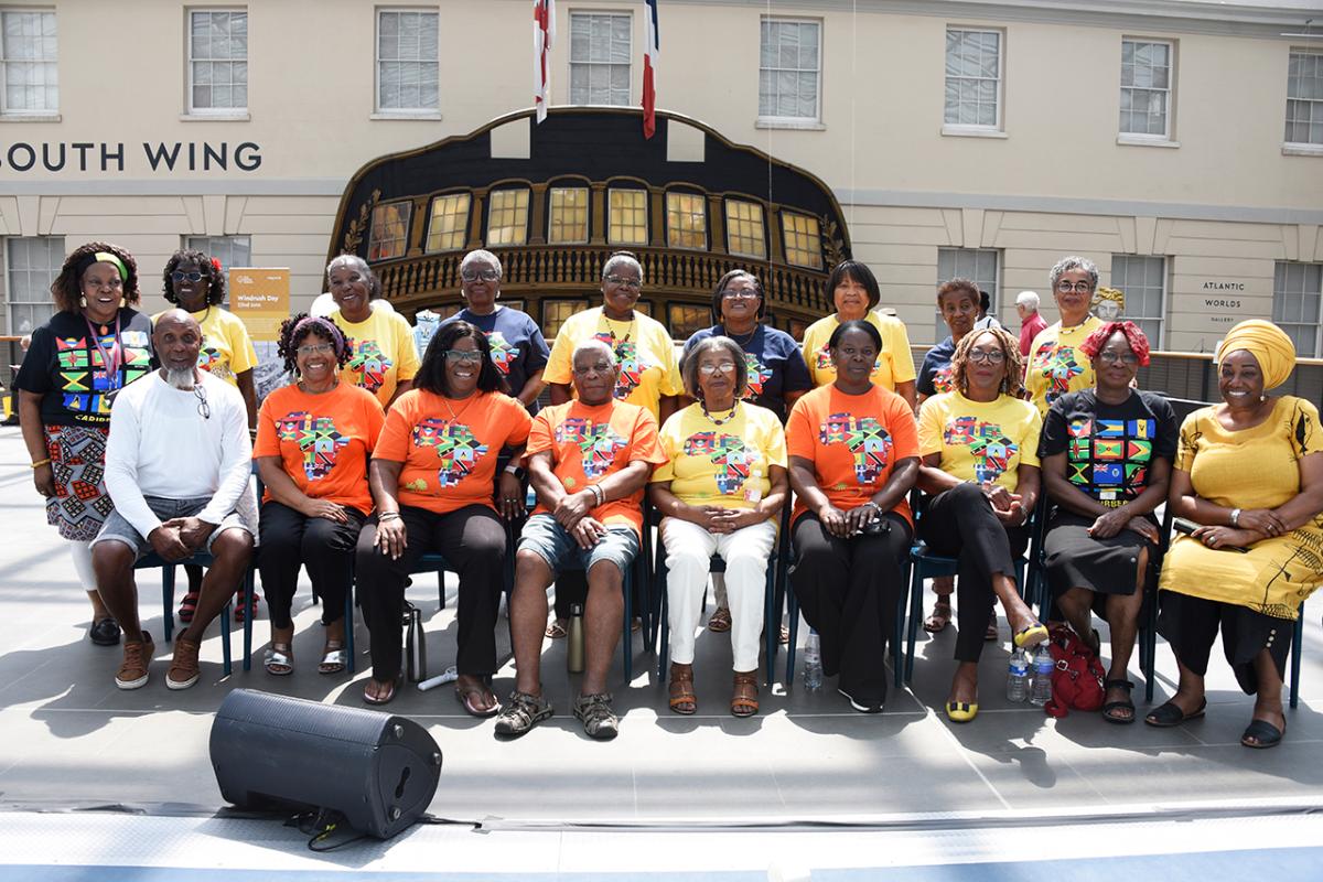 A group of men and women pose for a photo together in the National Maritime Museum. They are wearing t-shirts featuring different flags of countries in the Caribbean
