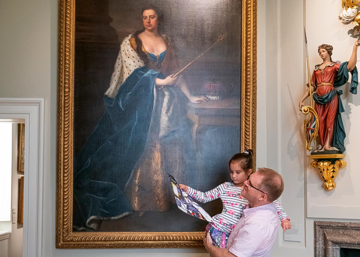 A father and daughter look up at a painting of Queen Anne in the Queen's House in Greenwich