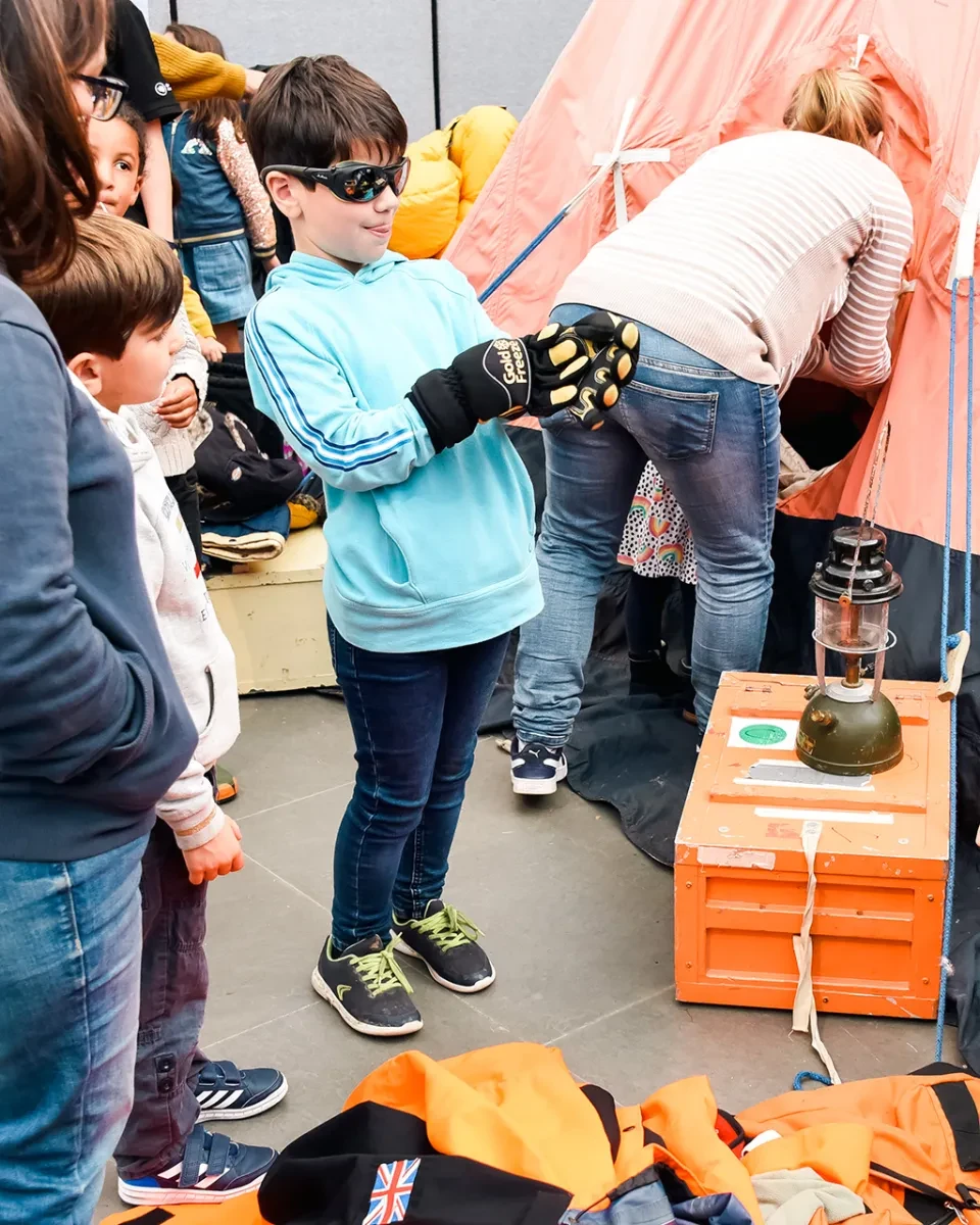 A boy tries on a pair of gloves and snow goggles during a demonstration of polar science equipment at the National Maritime Museum