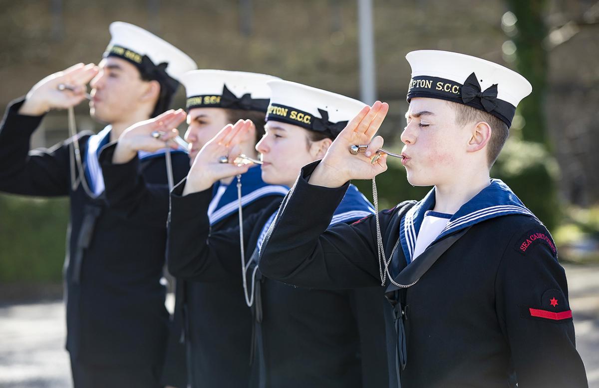 A group of sea cadets in naval uniform blow on a boatswain's whistle