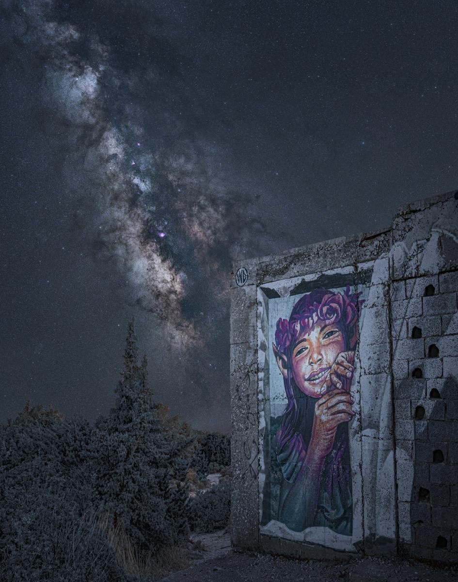 Image of graffiti of girl on wall with the Milky Way diagonal in the sky behind