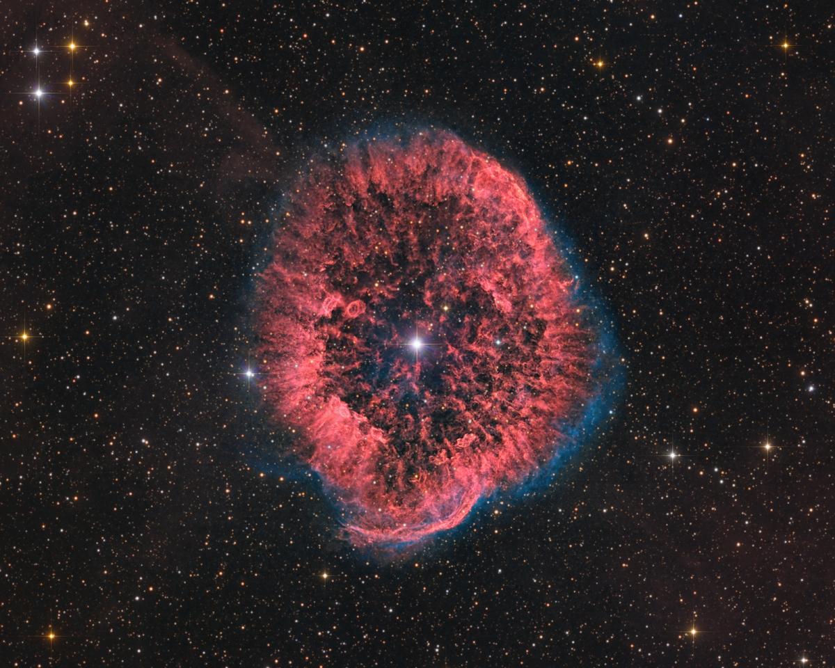Image of circular shaped nebula in red with a blue outline, with a very bright star at the centre