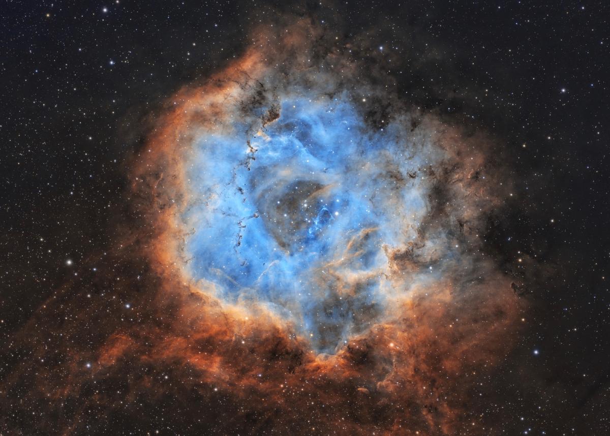Deep space image showing the Rosette Nebula, a beautiful cloud of bright blue gas surrounded by a halo of yellow and orange light