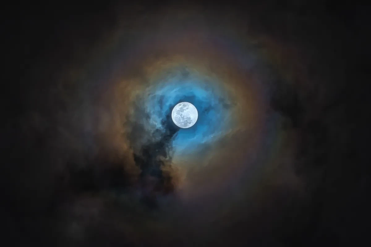 White full Moon surrounded by a ring of blue and orange hazy clouds