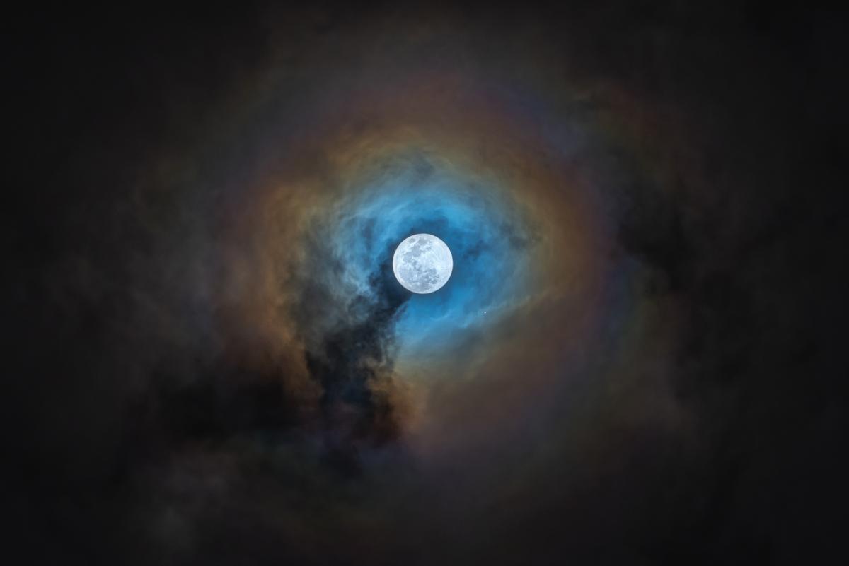 White full Moon surrounded by a ring of blue and orange hazy clouds