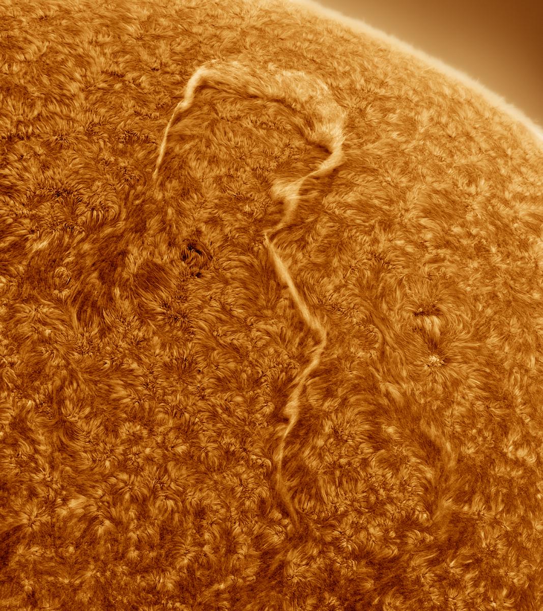 A close-up view of the Sun's surface taken using a telescope. The boiling orange surface includes a yellow flare that looks a little like a question mark