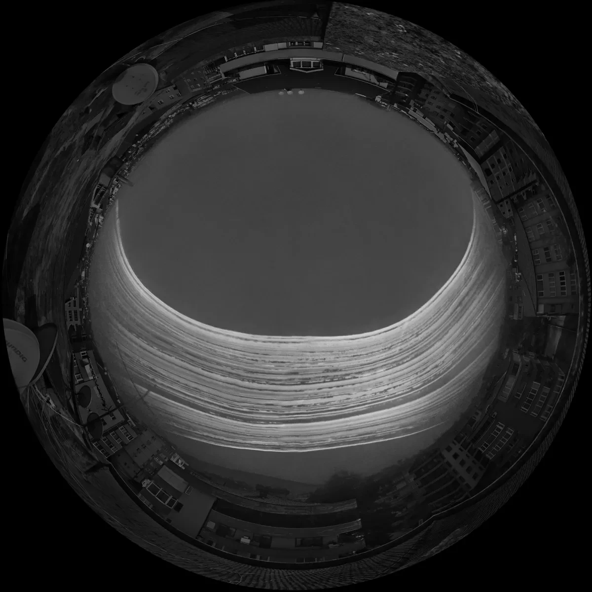An artistic black and white fish eye view photograph, showing a cityscape as a 'circle' in the frame. In the middle of the circle, multiple bright white lines of light show where the Sun has passed on different days over the course of the photo's exposure