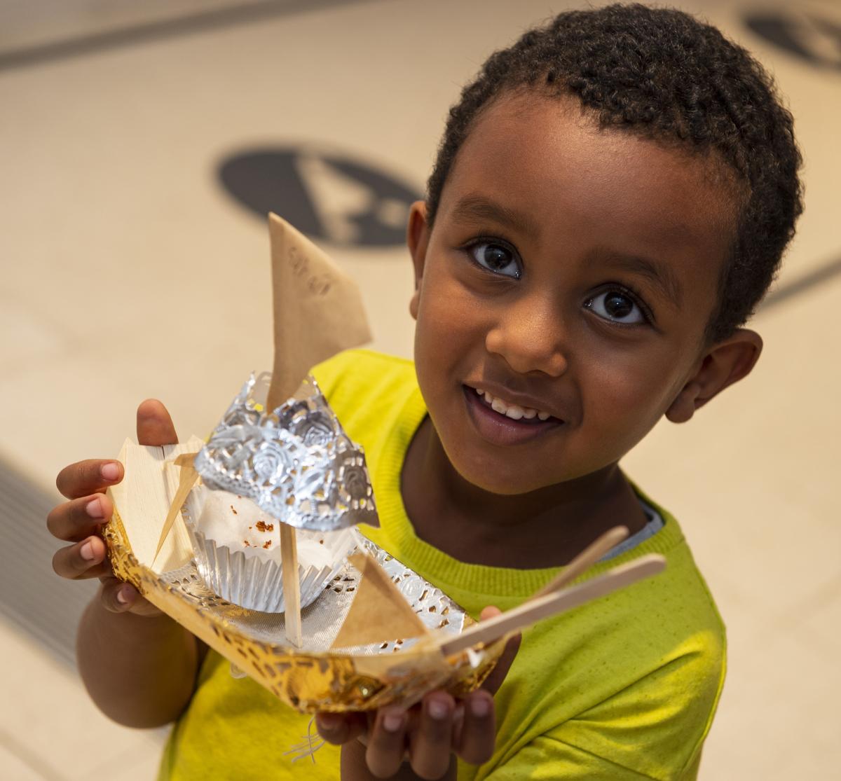 A young boy holds a homemade boat.