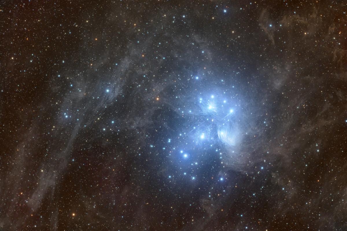 Image showing the Pleiades star cluster which features many bright blue glowing stars, with a reflection nebula around them reflecting the blue colour to make a blue glow