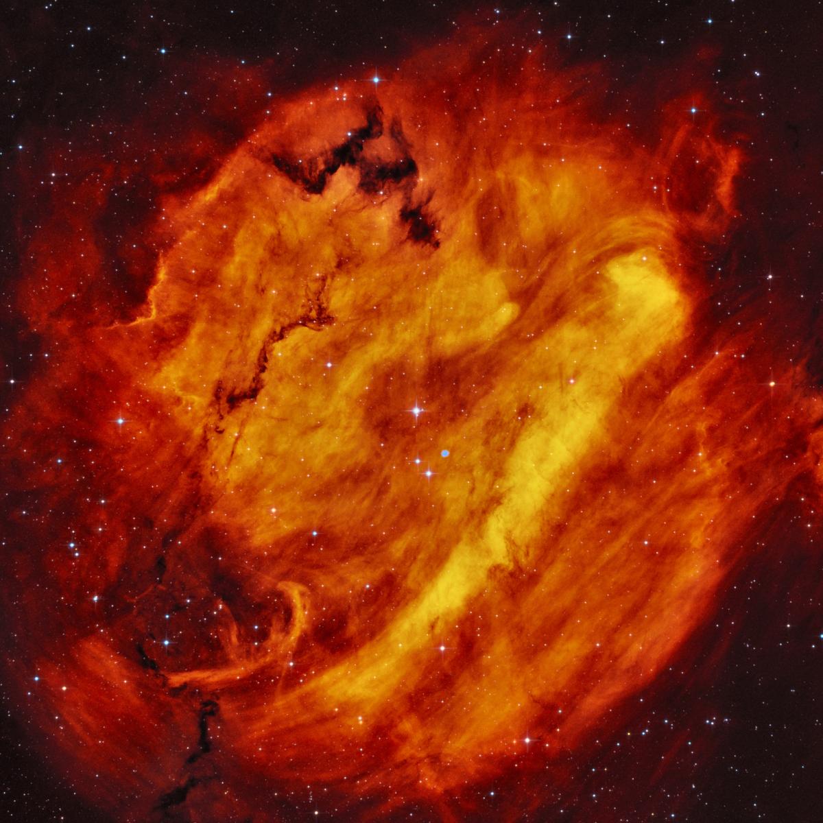 Image showing a nebula that resembles a flame, with big swirling clouds of reds, hot oranges, and yellows against a black starry night sky