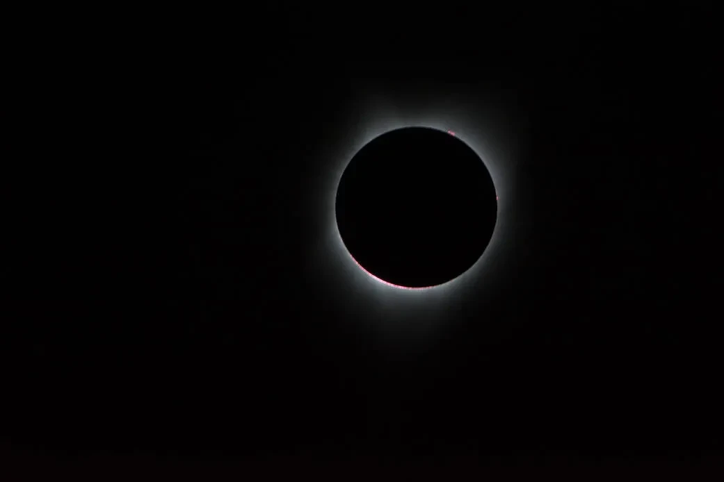 Image of the Sun with the Moon in front of it, with solar corona coming out from behind the circular Moon