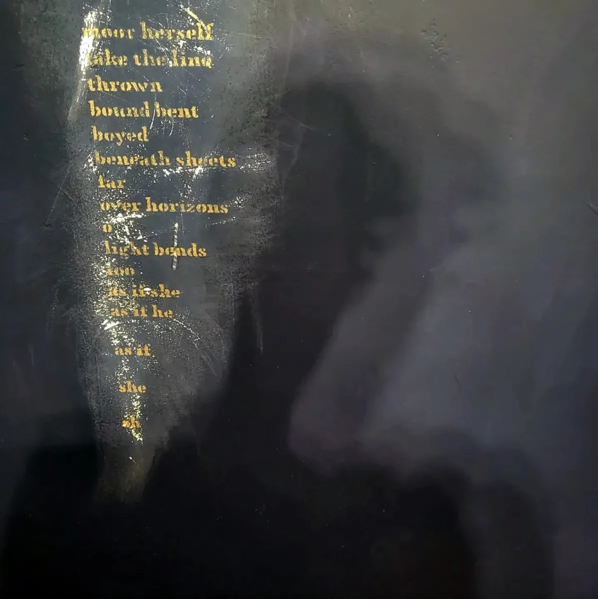 A photo abstracted by smoke clouds that shows the shadow of someone's head and shoulders in the centre and gold blurred writing on the left