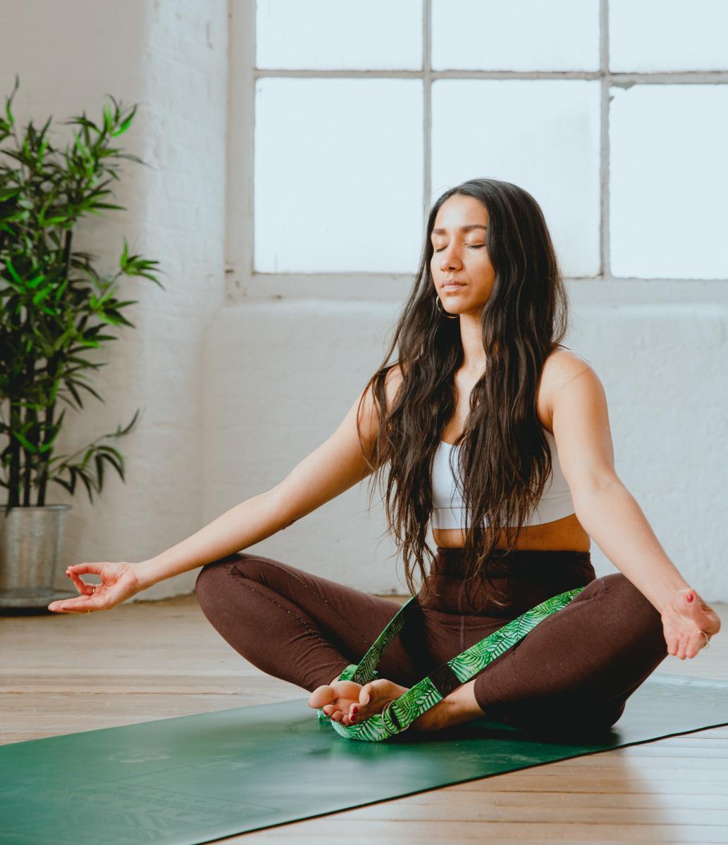 Image of woman in yoga pose sitting on map with feet touching and arms resting on knees with her eyes closed