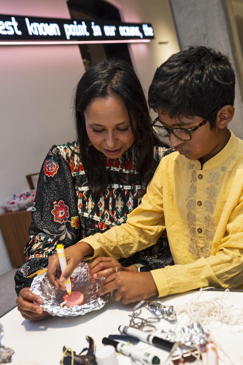 Child making a diya for diwali using tin foil and pens