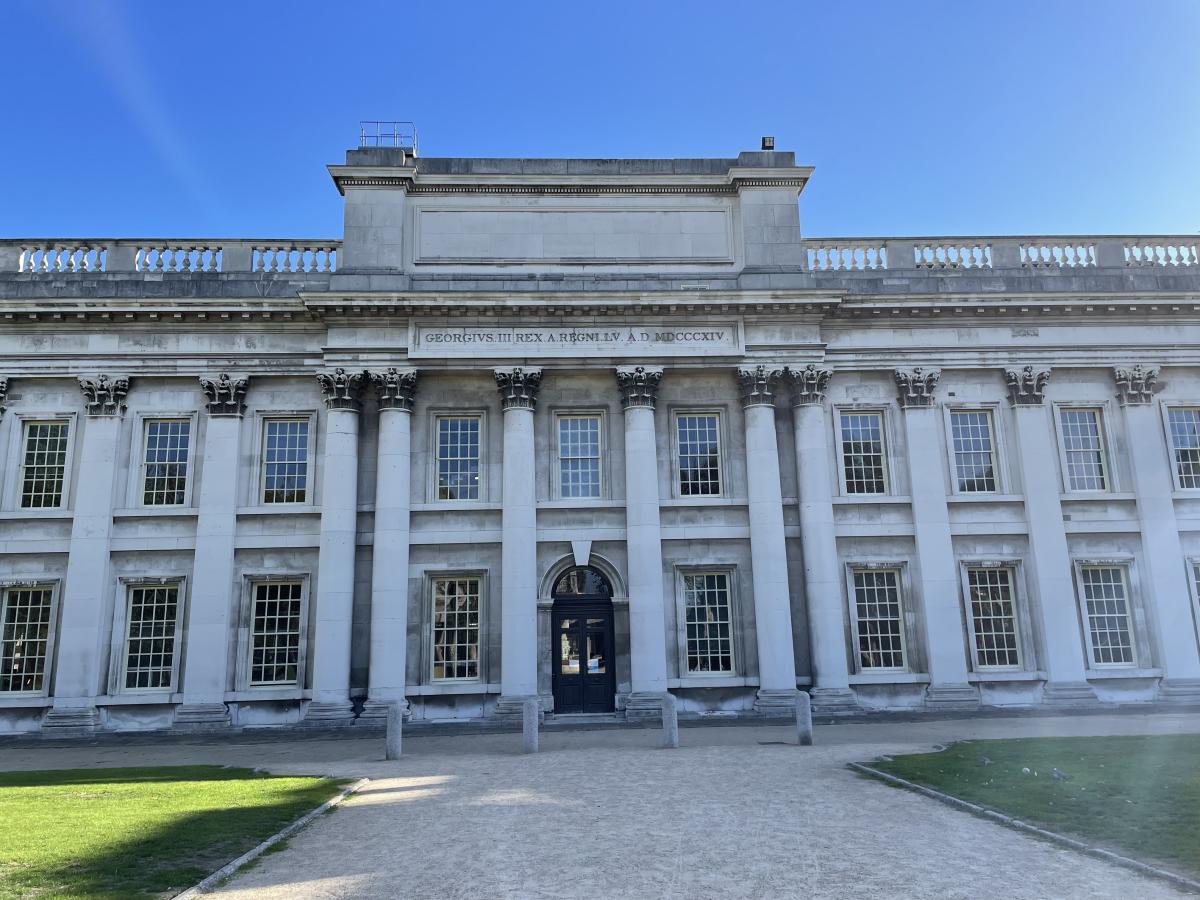 Photograph of part of the Old Royal Naval College in Greenwich. The grand building facade is made up of columns and high windows, with a dedication to King George III running along the top of the building