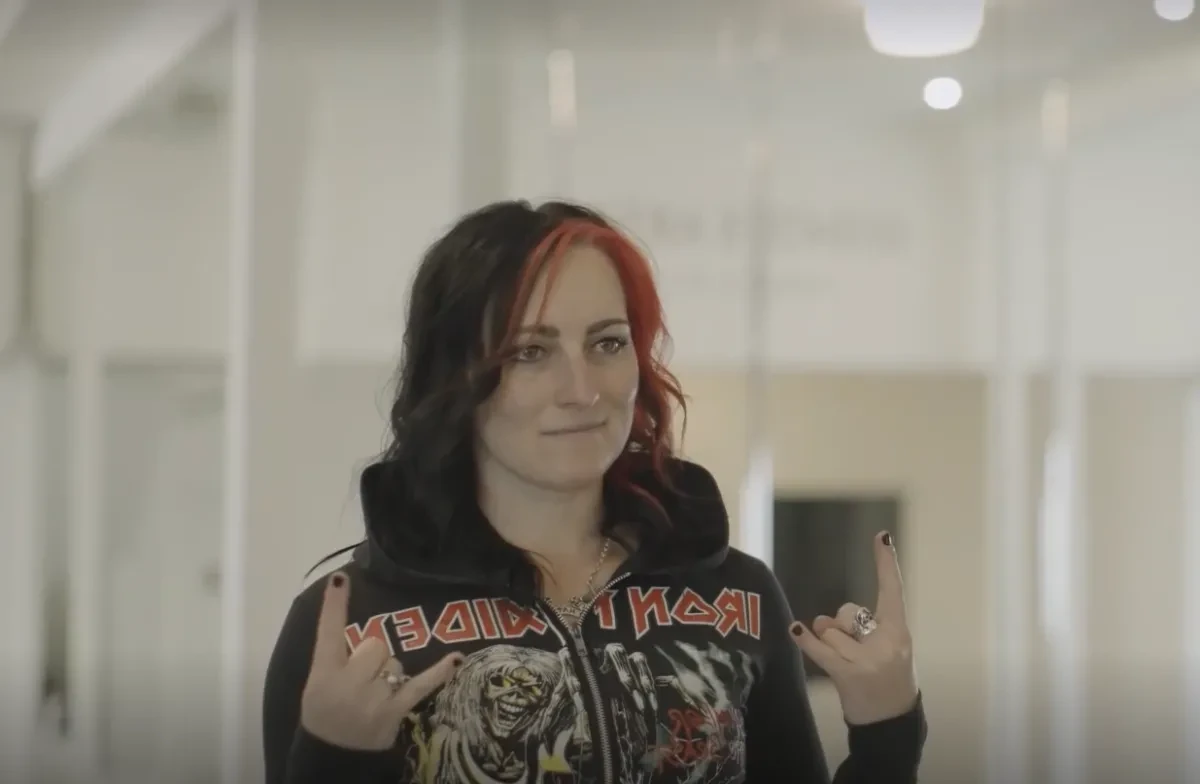 Image of woman with black and red hair wearing an Iron Maiden hoodie, making a metal symbol with her hands