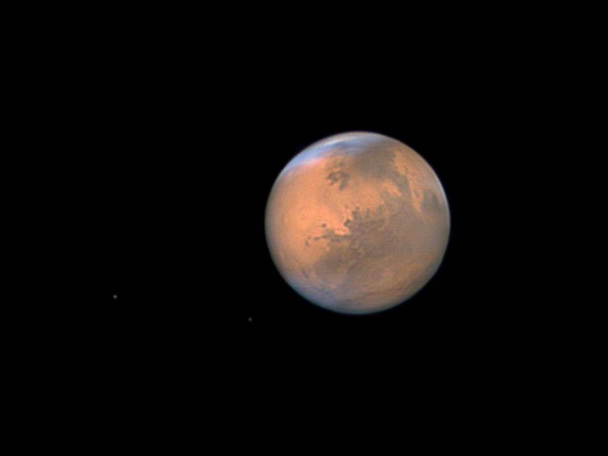 Telescope view of the planet Mars. The surface of the planet appears dusty orange against a dark black sky