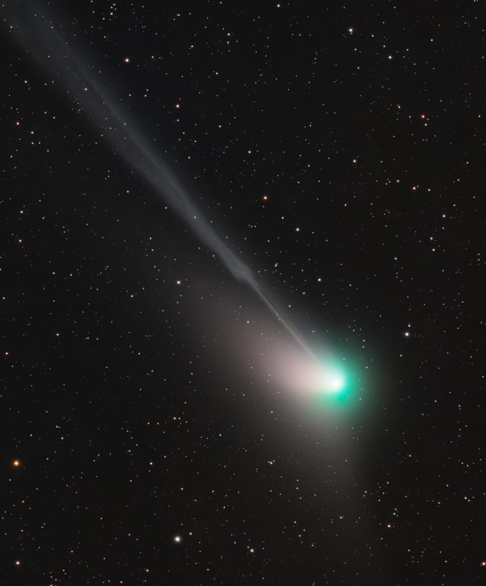Photograph of a comet taken using a telescope. The comet itself appears as a bright green light, with the tail streaming out diagonally behind