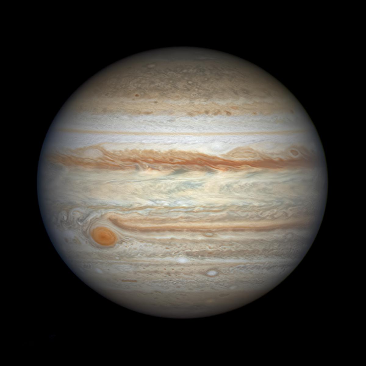 A close-up telescope view of the planet Jupiter, showing the planets swirling gases in remarkable detail. Swirling orange lines move horizontally across the planet's surface, along with hazy bands of yellow and white