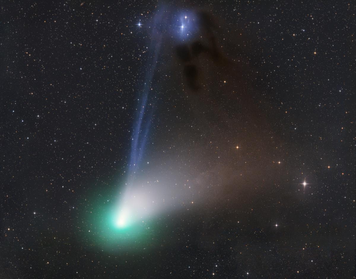 Photograph of a comet taken using a telescope. The comet appears at the bottom of the frame coloured bright green, with a pale blue shaft of light streaming behind. 