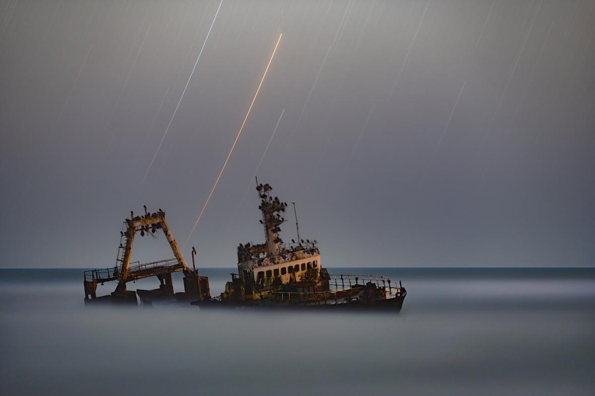Shipwreck surrounded by mist with star trails above