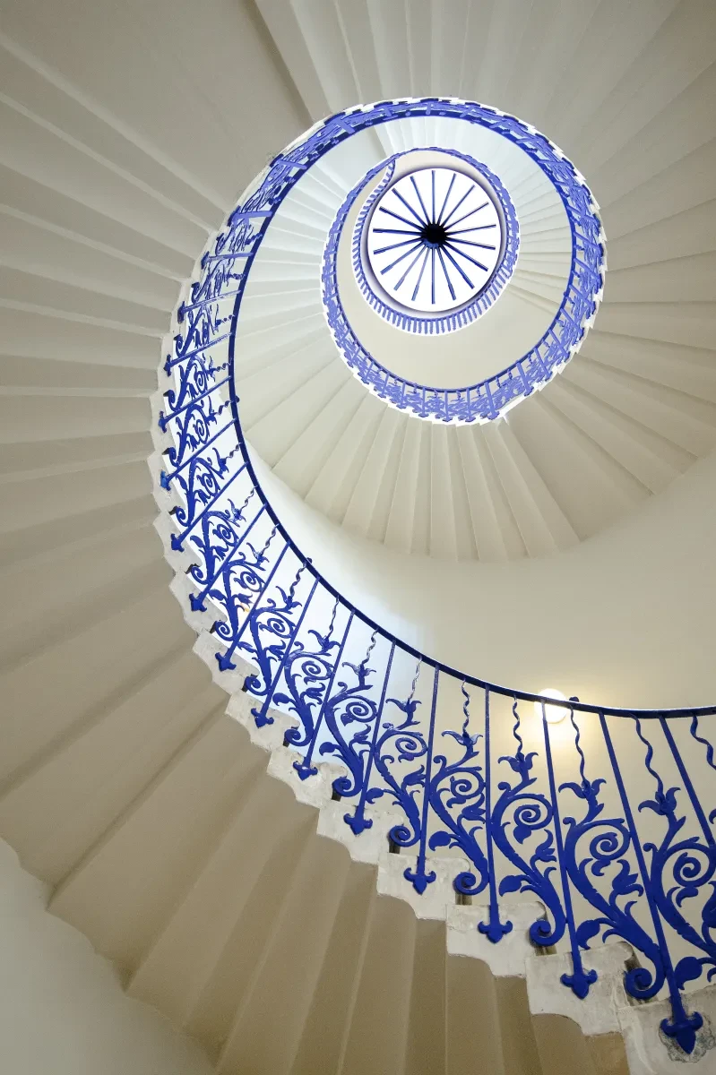 A white spiral staircase with a blue balustrade with tulip details