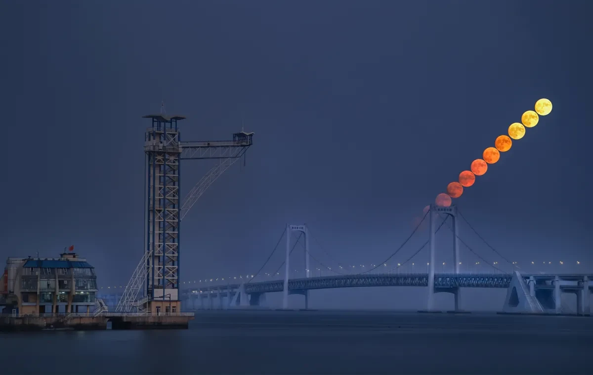 Moon rising over a bridge by the sea
