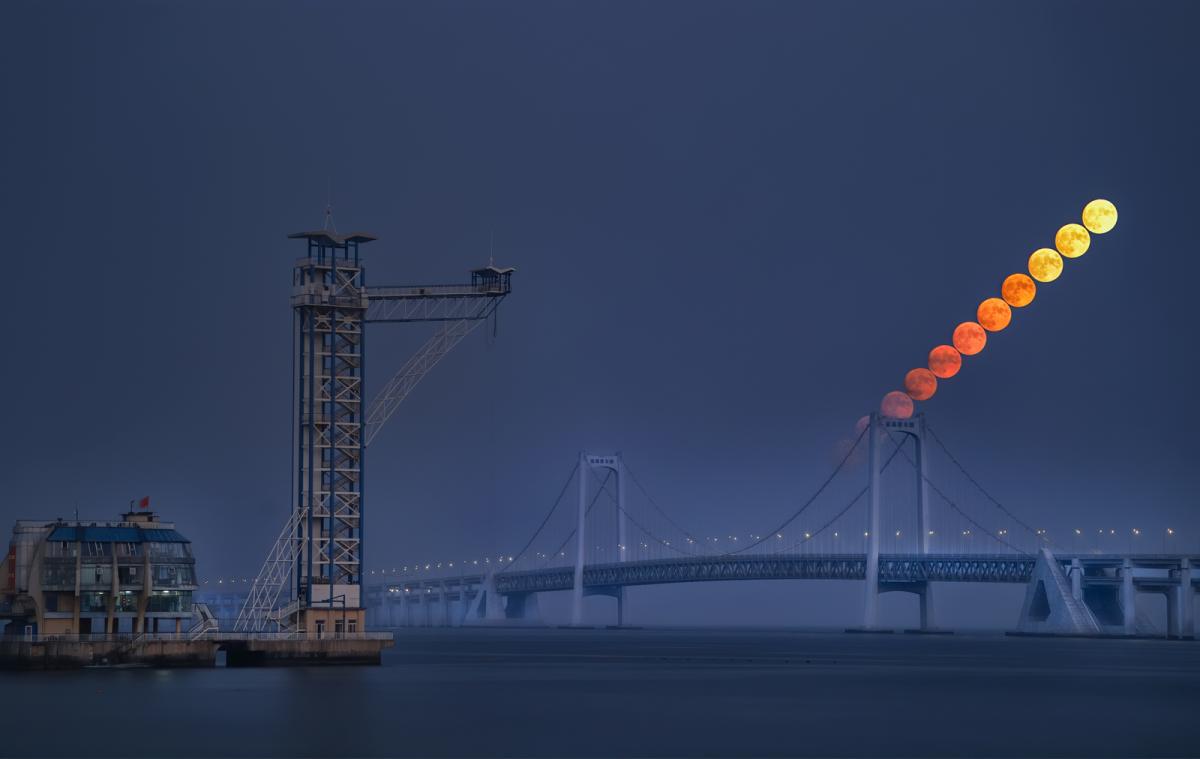 Moon rising over a bridge by the sea