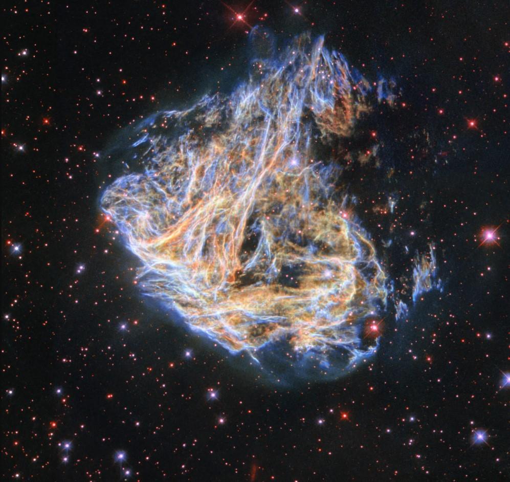 Image of supernova remnant which looks like a flame in the night sky, with short waves of blue and yellow all merged