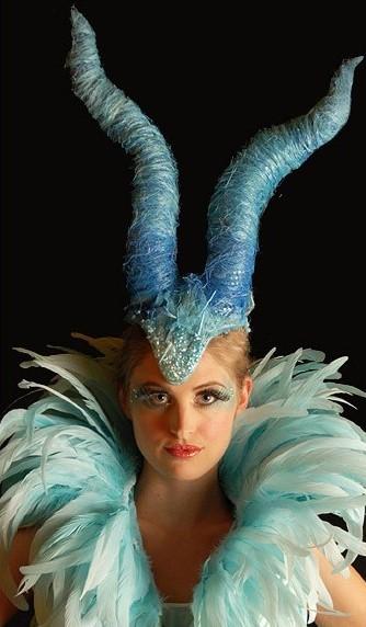 Image of a woman dressed as an ice fairy, wearing very long blue horns on her head and a big feather collar