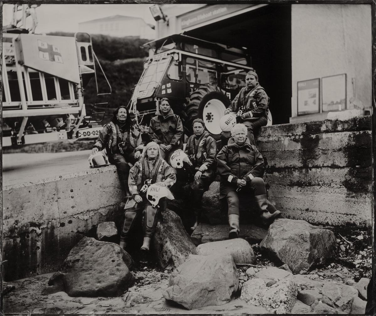 Black and white photograph of a group of lifeboat volunteers sitting on a slipway in front of a tractor